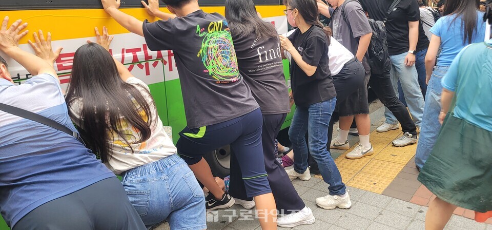 하차후 쓰러져 버스바퀴에 낀 할머니를 구하기 위해 현장에 있던 주민들이 버스를 밀고 있다.